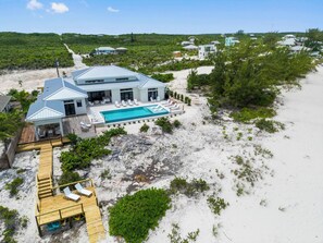 Ett stort hus med en swimmingpool, en träterrass och utsikt över stranden.