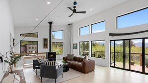 Un salon spacieux doté d’une cheminée, de grandes fenêtres et d’un balcon offrant une vue sur les montagnes.