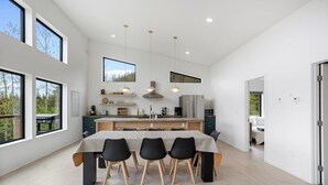Une cuisine moderne dotée d’un îlot central, de luminaires suspendus et de grandes fenêtres offrant une vue sur l’extérieur.