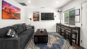 A modern living room with a dark sofa, a coffee table, and a patterned rug. There are two wall-mounted TVs and a large painting above the sofa. - Barrel Retreat in the Heart of Downtown Phoenix (Phoenix)