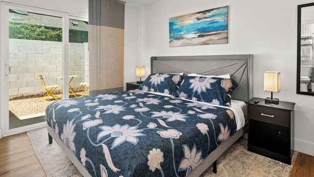 A bedroom with a large bed, a nightstand, a lamp, a painting, and a sliding glass door leading to an outdoor area. - Barrel Retreat in the Heart of Downtown Phoenix (Phoenix)