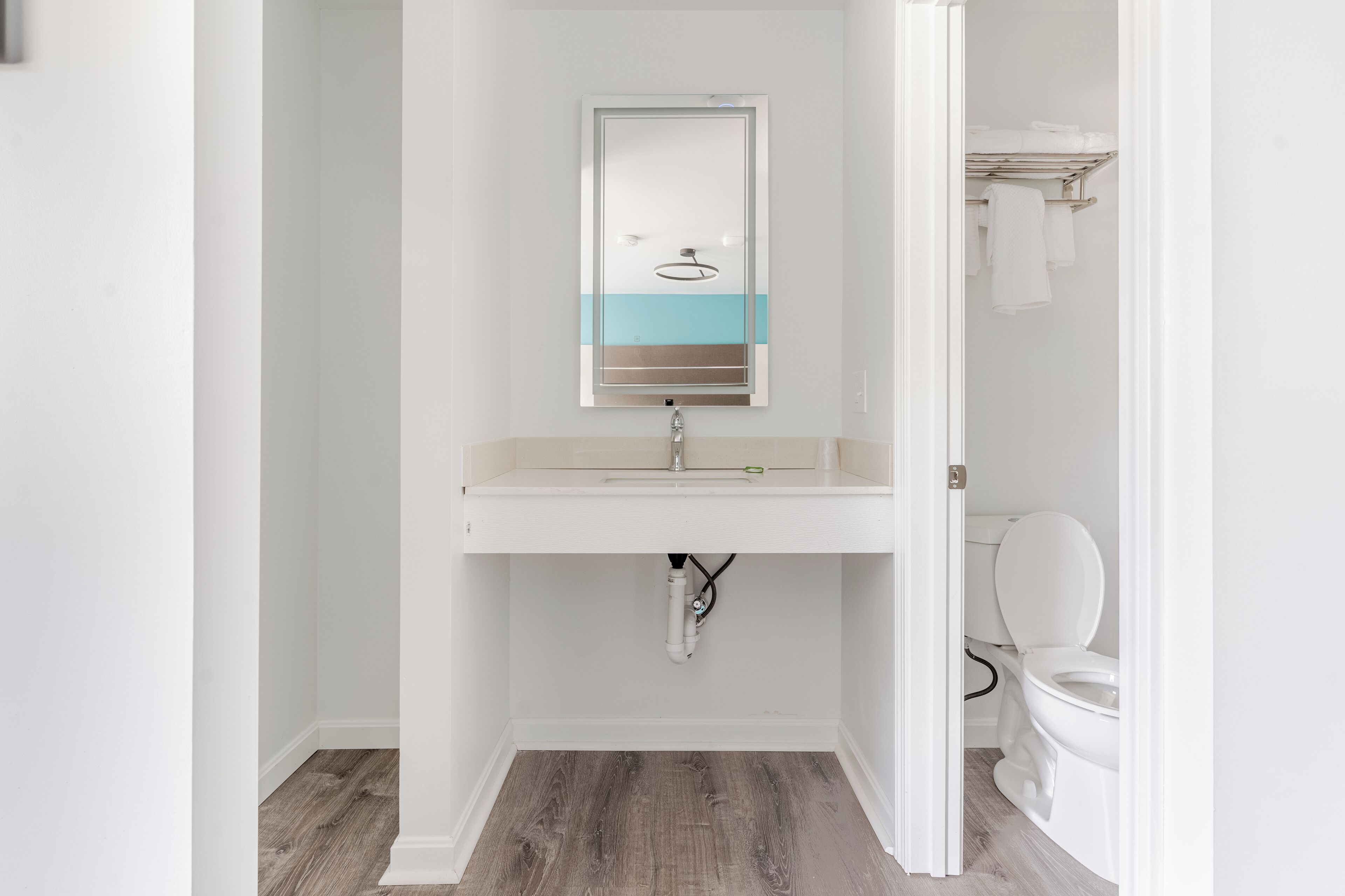 Un baño con lavamanos blanco, espejo y retrete.