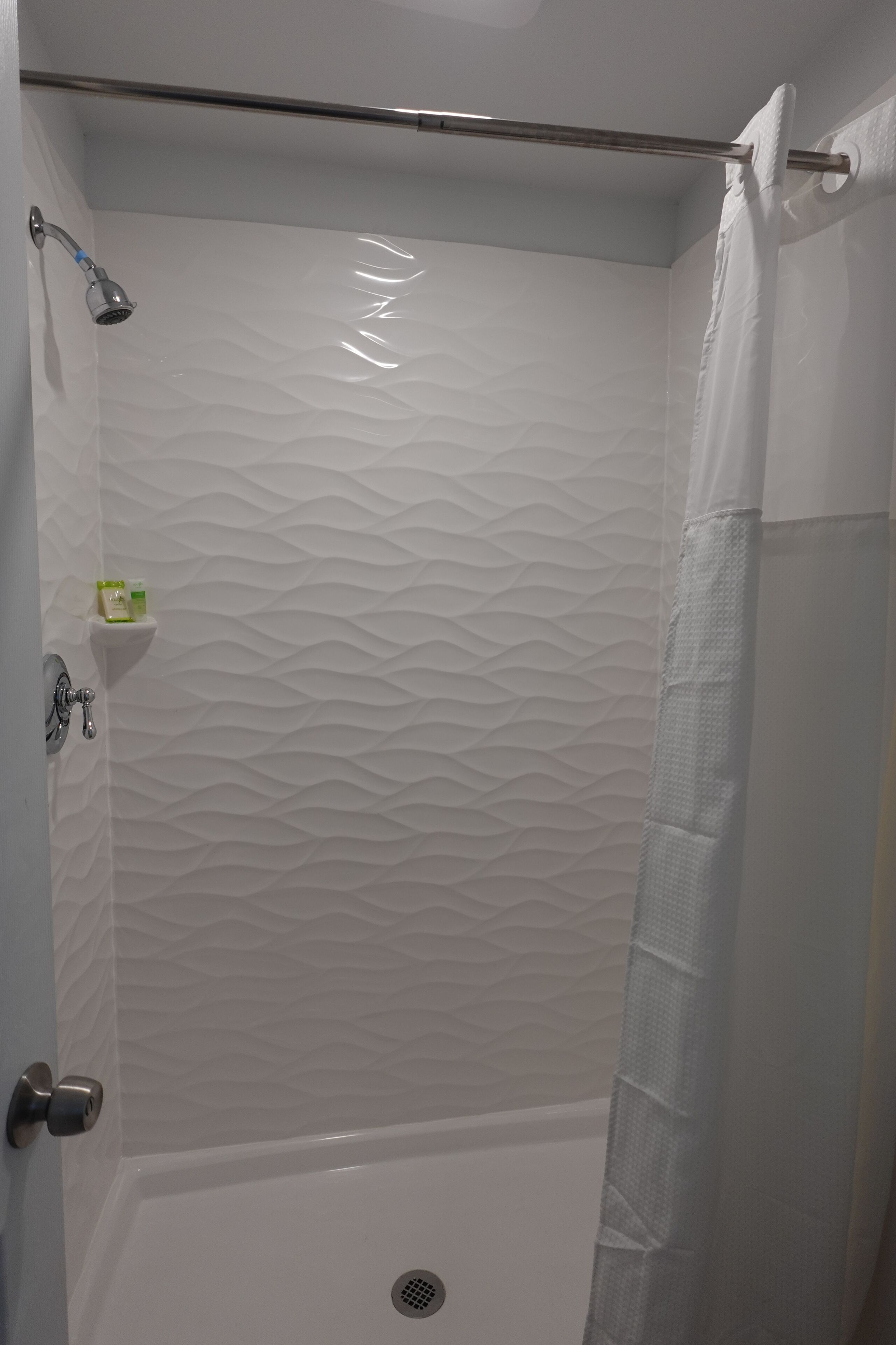 A shower with a textured wall, a metal showerhead, a towel bar, and a small shelf with toiletries.