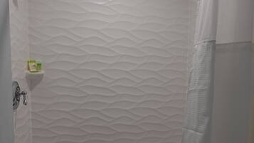 A shower with a textured wall, a metal showerhead, a towel bar, and a small shelf with toiletries.