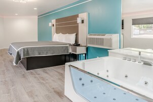 Una habitación de hotel moderna con una bañera grande, una cama con colcha gris y una pared de acento azul.