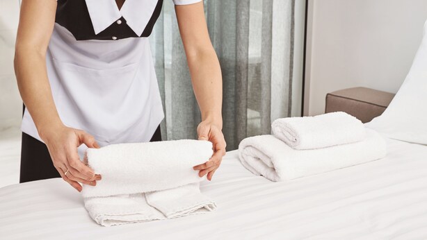 A person folding towels on a bed in a hotel room. - Blue Beach Motel (North Kingstown)