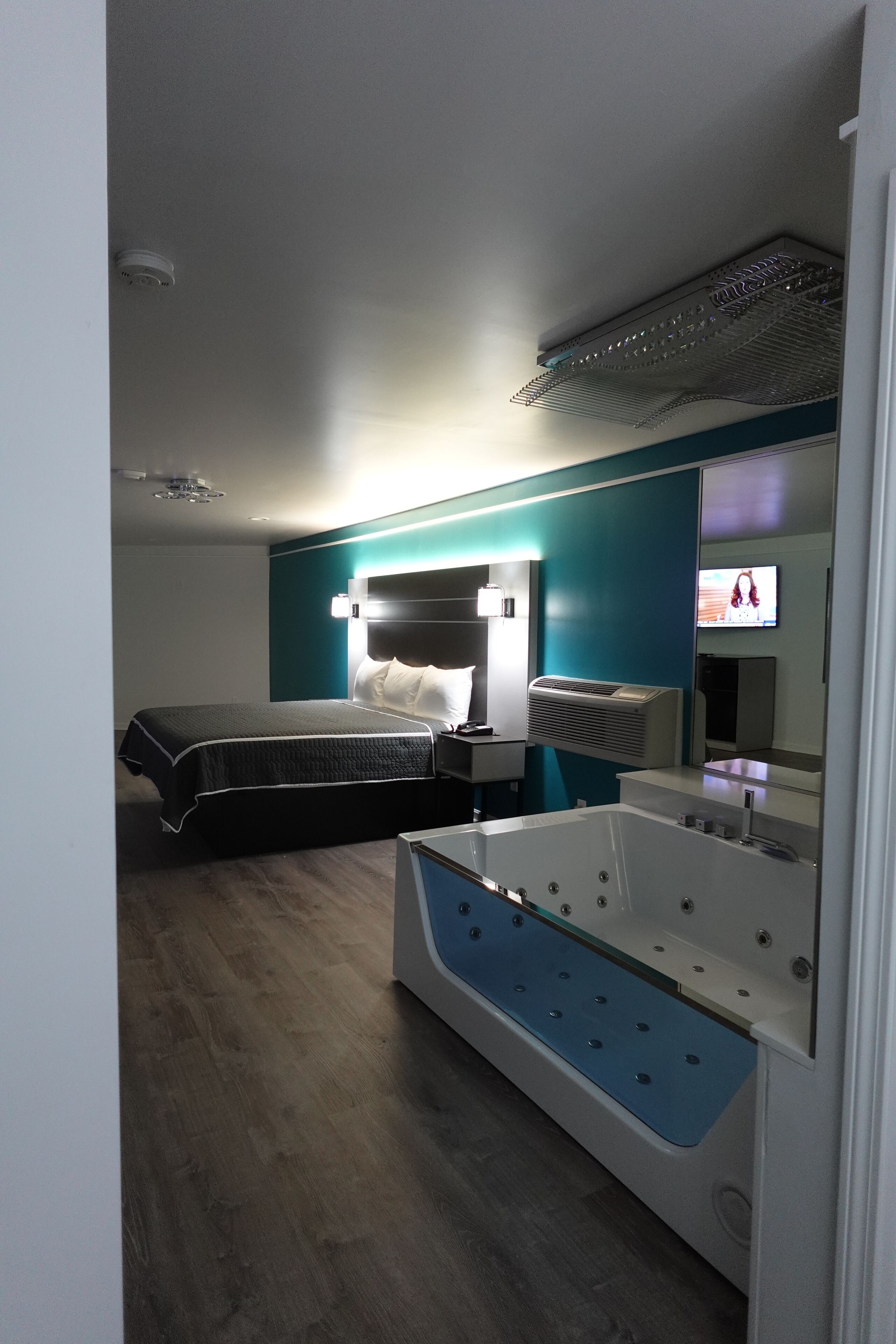 Habitació d'hotel moderna amb un llit gran, zona de seients separada amb una banca blava, banyera integrada i televisió penjada a la paret.