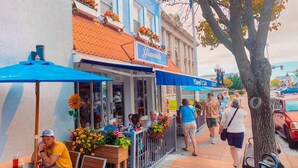 A street-side café with outdoor seating, a blue awning, and a building with a blue and white facade.