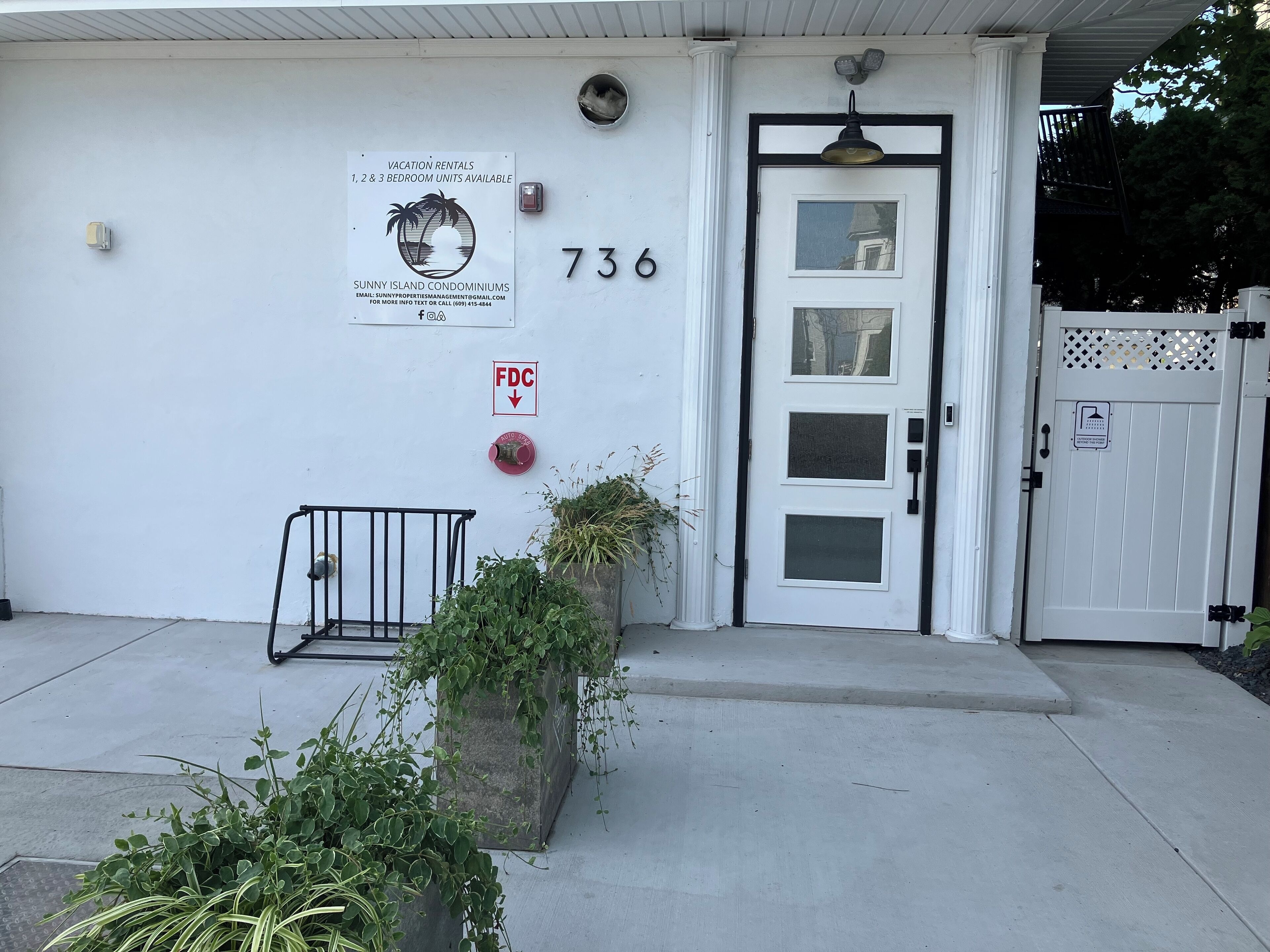 A white building with a door marked "736" and a sign for Sunny Island Condominiums offering vacation rentals.