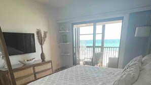 Une chambre avec un lit, une télévision, une commode et un balcon donnant sur la mer.