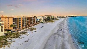 Un hôtel situé en bord de mer, doté d’une longue plage de sable, offrant une vue sur l’océan, et bordé d’une rangée de bâtiments le long du littoral.