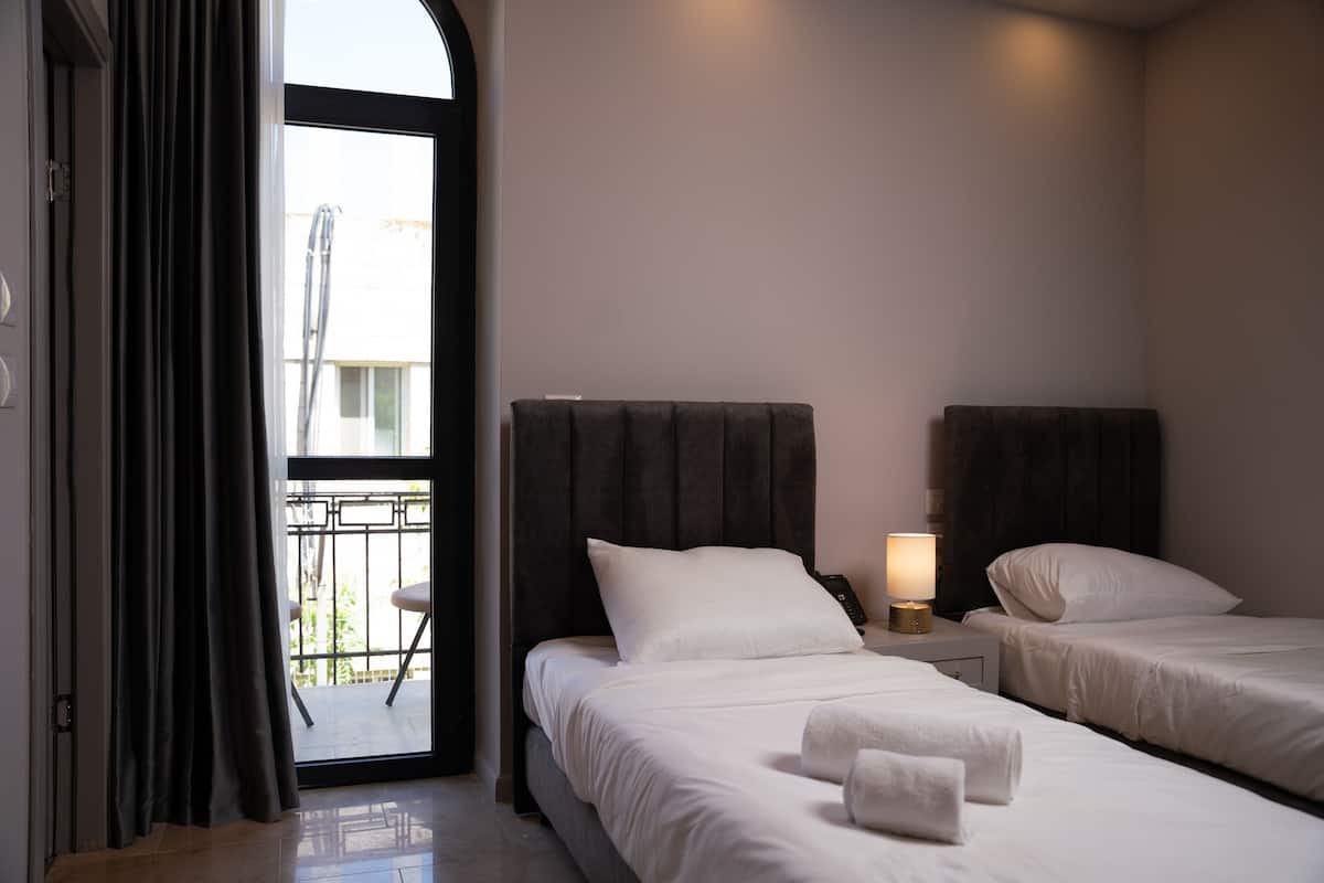 A hotel room with two beds, a balcony, and a nightstand with a lamp.