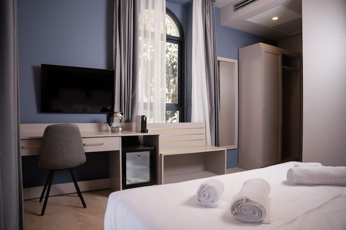A hotel room with a bed, a desk, a chair, a television, a wardrobe, and a window with curtains.