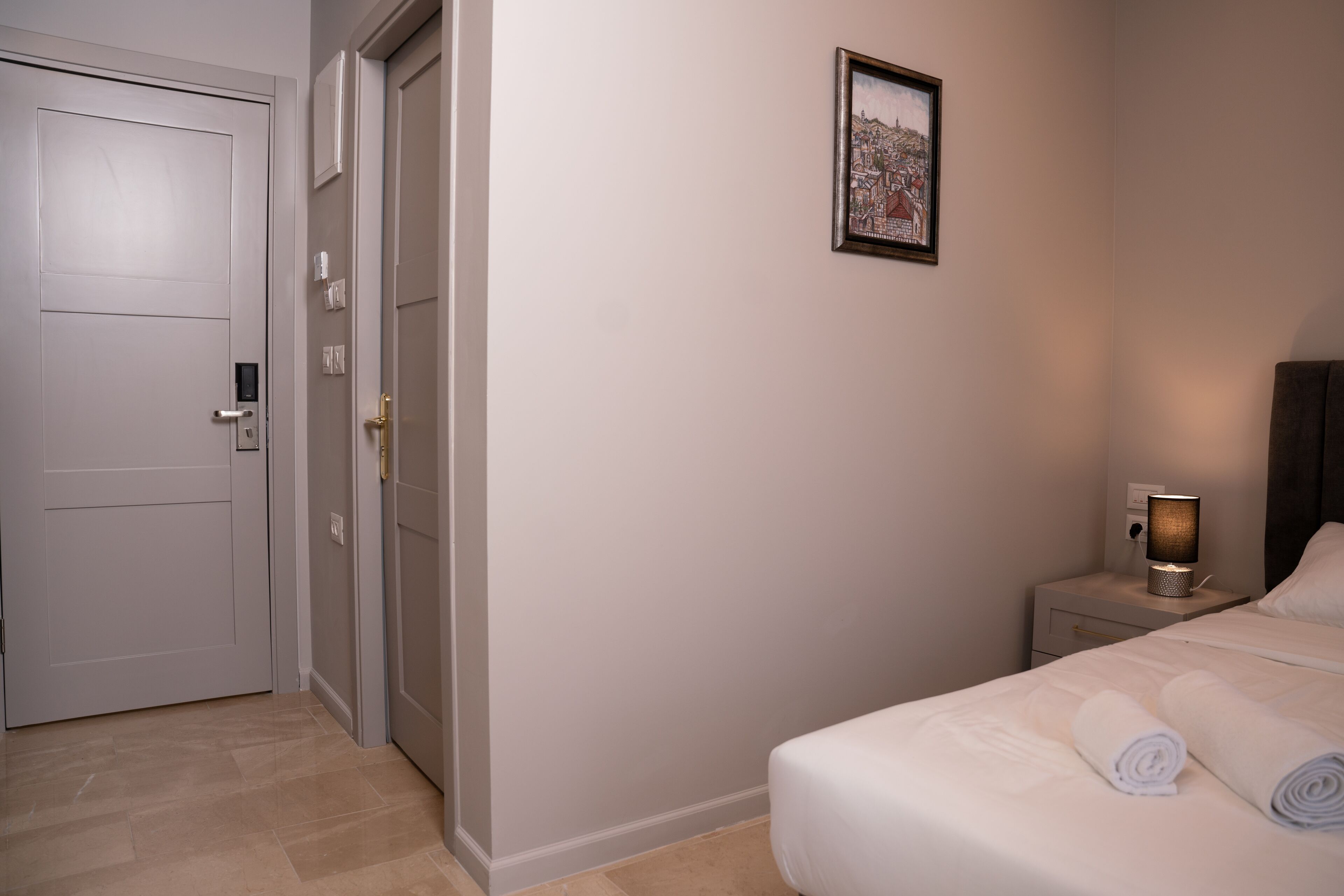 A hotel room with a bed, a nightstand with a lamp, a door, and a framed picture on the wall.