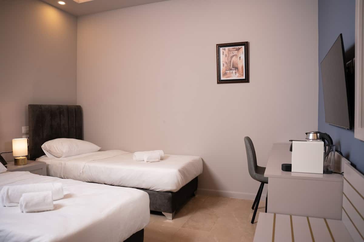 A hotel room with two beds, a desk, a chair, a lamp, and a framed picture on the wall.