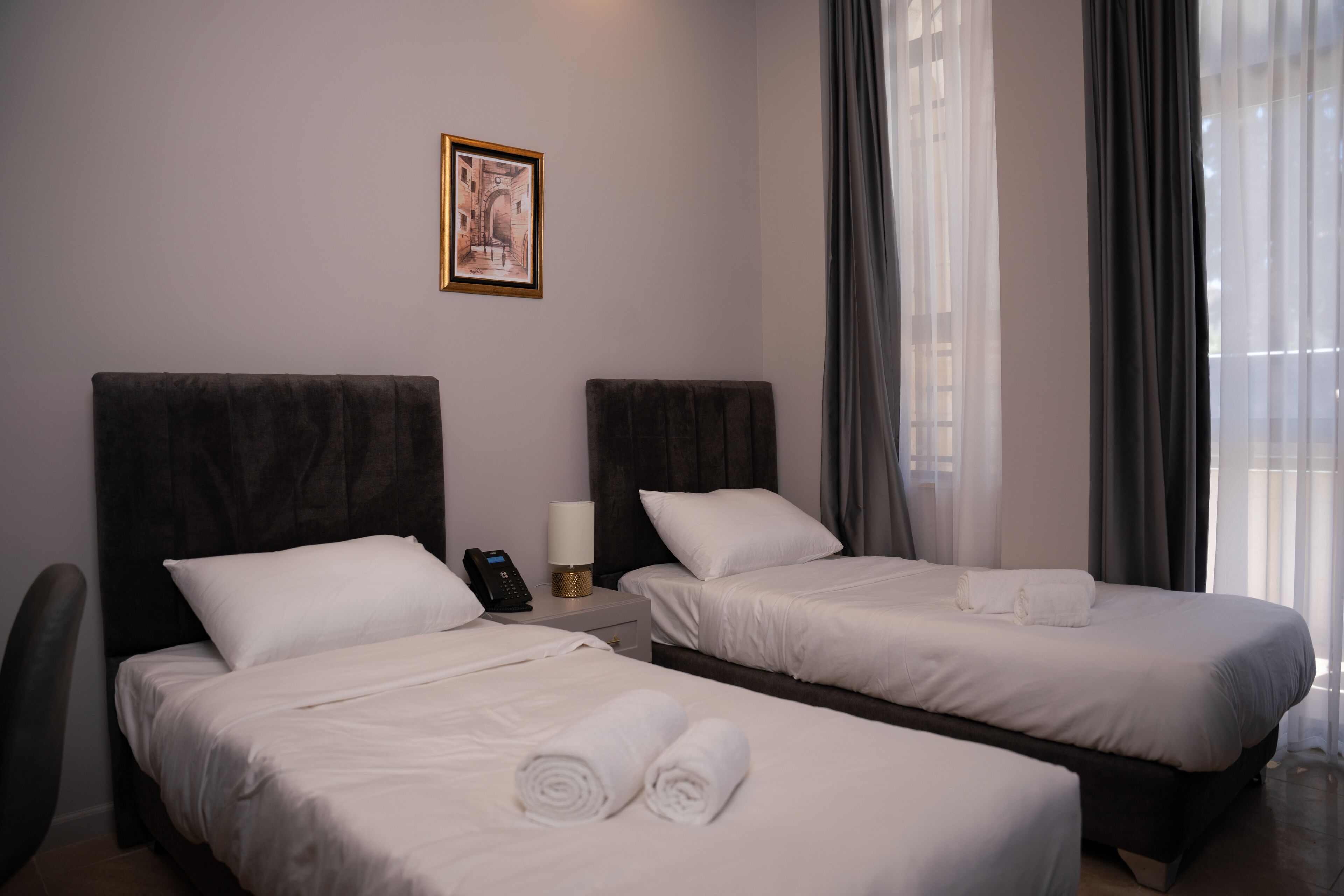 A hotel room with two beds, a nightstand with a phone, a lamp, and a framed picture on the wall.