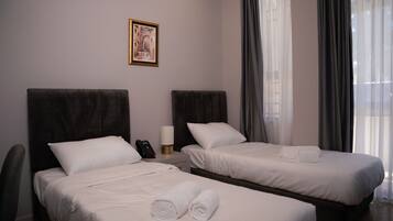 A hotel room with two beds, a nightstand with a phone, a lamp, and a framed picture on the wall.