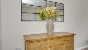 Une commode en bois sur laquelle est posé un vase de fleurs, un miroir au-dessus et une prise électrique en dessous.