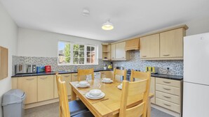 Une cuisine moderne avec des meubles en bois, une table à manger pour quatre personnes et une fenêtre laissant entrer la lumière naturelle.