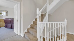 Un escalier avec des balustrades blanches et des marches recouvertes d’une moquette beige, menant à un palier.