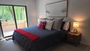 A bedroom with a bed, pillows, a nightstand, a lamp, and a window with a view of trees. - Trout Creek Unit 8, Beautiful newly Decorated Very Clean Condo , Building 2 (Harbor Springs)