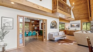A spacious living area with a high ceiling, wooden beams, a dining area with a view, and a cozy seating area with a cowhide rug.