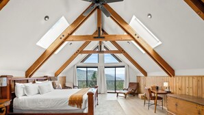 A bedroom with a large bed, wooden beams, a desk, and a view of the outdoors.