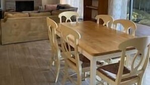 Een eetgedeelte met een houten tafel en witte stoelen, een bank en een open haard.