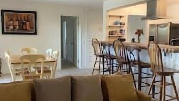 Een woonkamer met een bank, een eettafel en stoelen. Er is een keukenhoek met een aanrecht en kastjes.