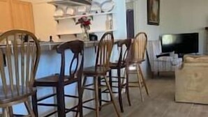 Een keuken met houten stoelen, een eettafel en een televisie in de woonkamer.