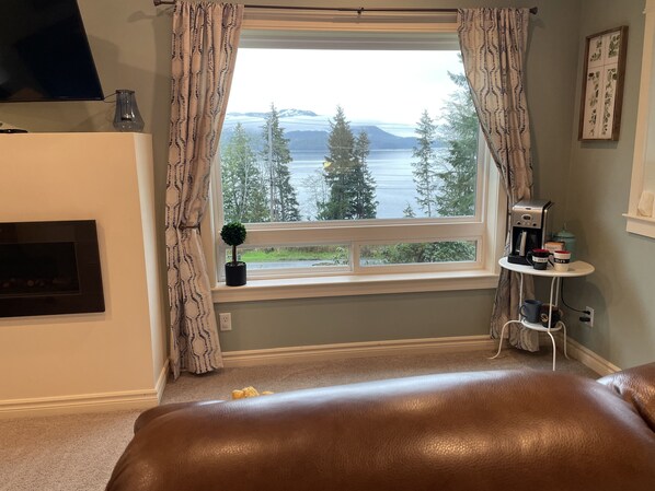 A bedroom with a large window, a fireplace, a coffee maker, and a small table with mugs.