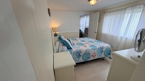 A bedroom with a bed, bedside table, lamp, and a fan.