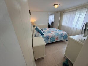 Una camera da letto con un letto, un comodino, una lampada e una ventola.