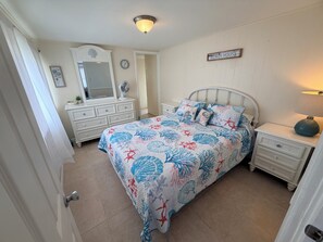 A bedroom with a bed, a dresser, a mirror, a bedside table, and a wall clock.