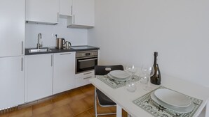 A modern kitchen with white cabinets, a stainless steel sink, an oven, and a dining table set with plates and glasses. - GuestHost - Amazing studio of 36 sqm, able to accommodate up to 3 people, located on the ground floor of a building in the quiet residential complex of Collina Fiorita. The property boasts a spacious terrace with fabulous views of Porto Sole and the avai (Sanremo)