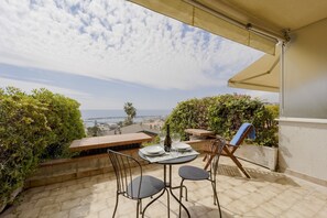 A terrace with a table set for two, chairs, a bottle, and glasses.