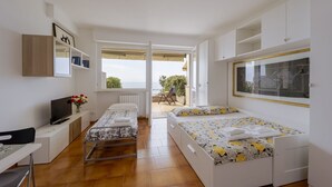 A compact room with a bed, a desk, a TV, and a view of the outdoors. - GuestHost - Amazing studio of 36 sqm, able to accommodate up to 3 people, located on the ground floor of a building in the quiet residential complex of Collina Fiorita. The property boasts a spacious terrace with fabulous views of Porto Sole and the avai (Sanremo)