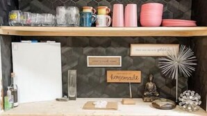 Une cuisine avec deux étagères en bois, un réfrigérateur blanc et un plan de travail sur lequel se trouvent divers ustensiles de cuisine.