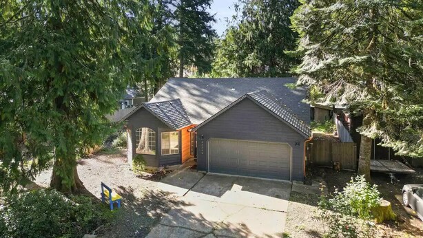 Une maison à deux étages avec un garage, entourée d’arbres et dotée d’une petite cour.
