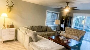 Un salon comprenant un canapé, un pouf, une table basse et une tête de cerf décorative accrochée au mur.