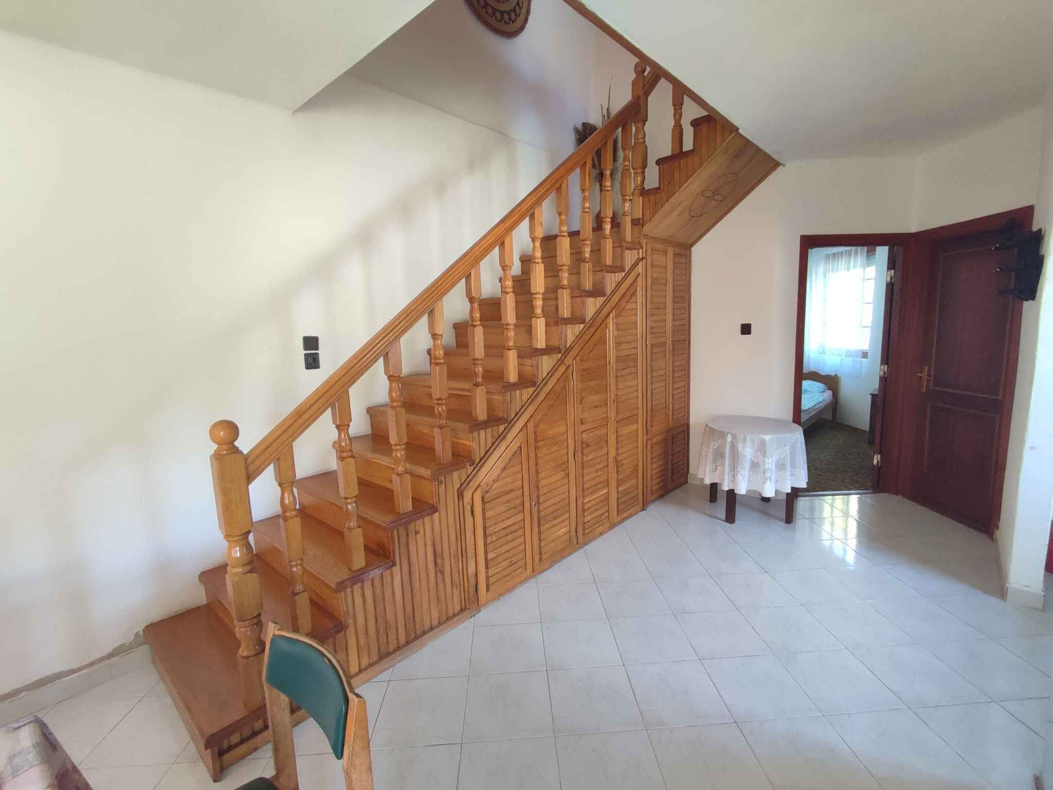 Eine Treppe mit Holzbalken und Holzlaufsteinen, ein runder Tisch mit weißer Tischdecke und eine Tür zu einem anderen Raum.