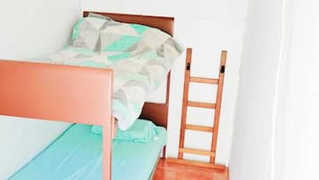 A small, single-bed room with a wooden frame, a green bedspread, and a ladder against the wall.