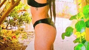 Una persona en traje de baño de pie en un espacio exterior exuberante, con mucha vegetación y una planta colgante.