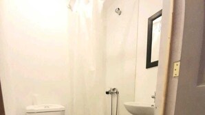 Un baño pequeño y funcional con inodoro, lavamanos e insonorizado para la ducha.