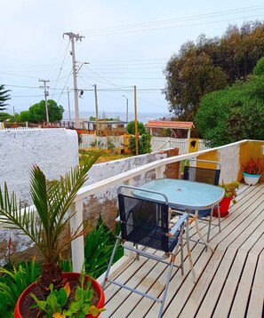 A wooden deck with a table and chairs, surrounded by potted plants and a white fence. - The Ocean Hostel (El Quisco)