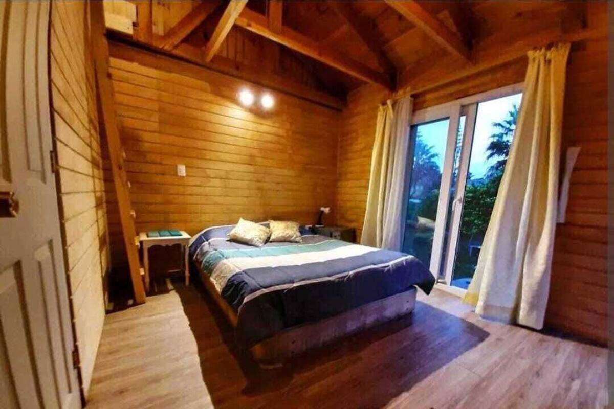 Ein Schlafzimmer einer Holzhütte mit einem Bett, einem Nachttisch und einem Fenster mit Vorhängen.