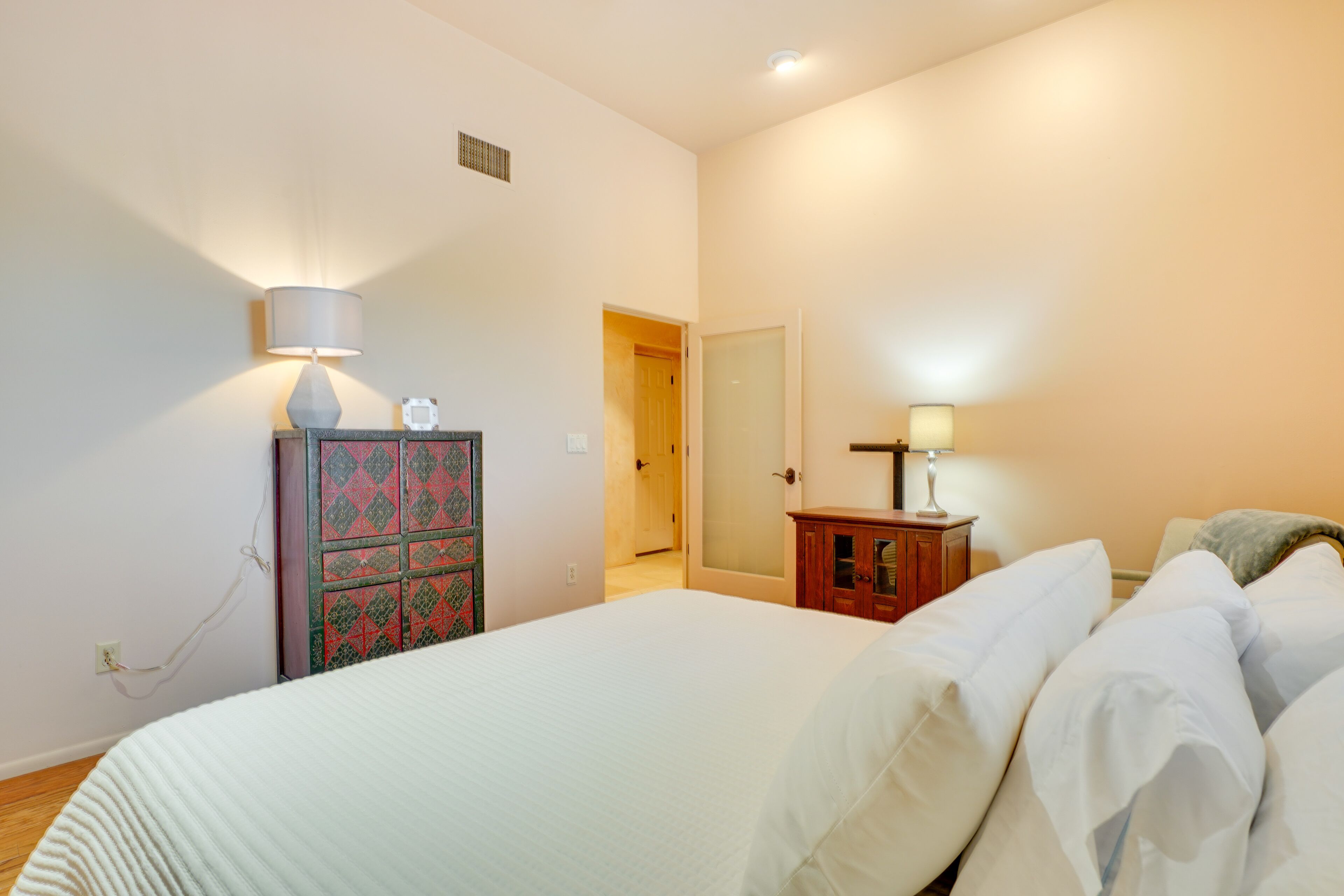 A bedroom with a large bed, a dresser, a lamp, and a door leading to another room.