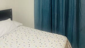 Une chambre avec un lit, un rideau bleu et un appareil de climatisation.
