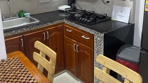 Une cuisine avec des meubles de rangement en bois, un plan de travail noir, une cuisinière à gaz et un évier.