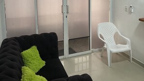 Une pièce avec un canapé noir, une chaise blanche et une porte-fenêtre coulissante donnant sur un balcon.